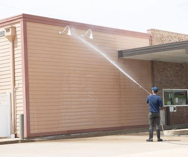 Person power washing the exterior wall of a building with two outdoor lights.