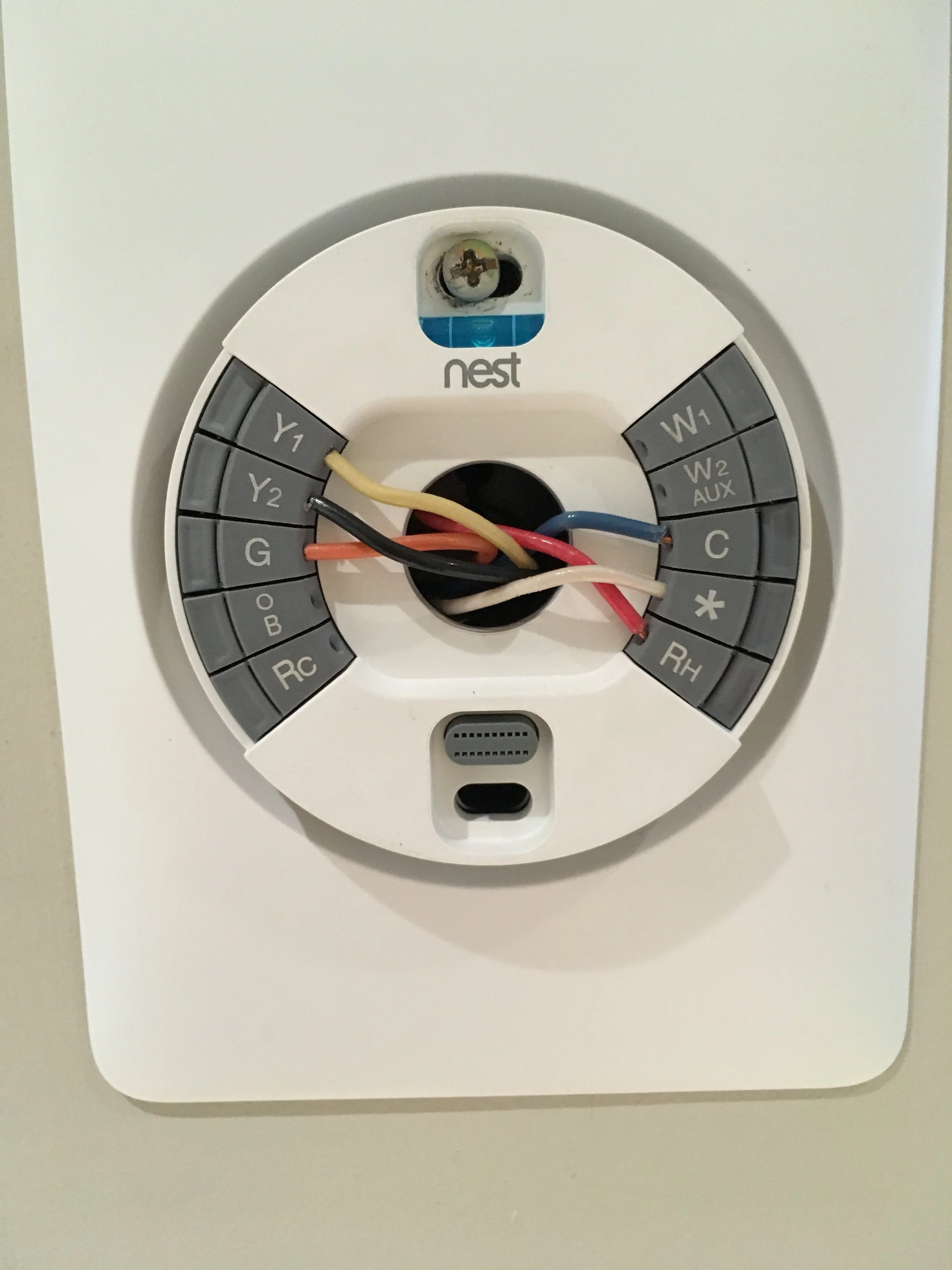 A circular Nest thermostat with multiple color wires connected to its terminals, mounted on a wall.