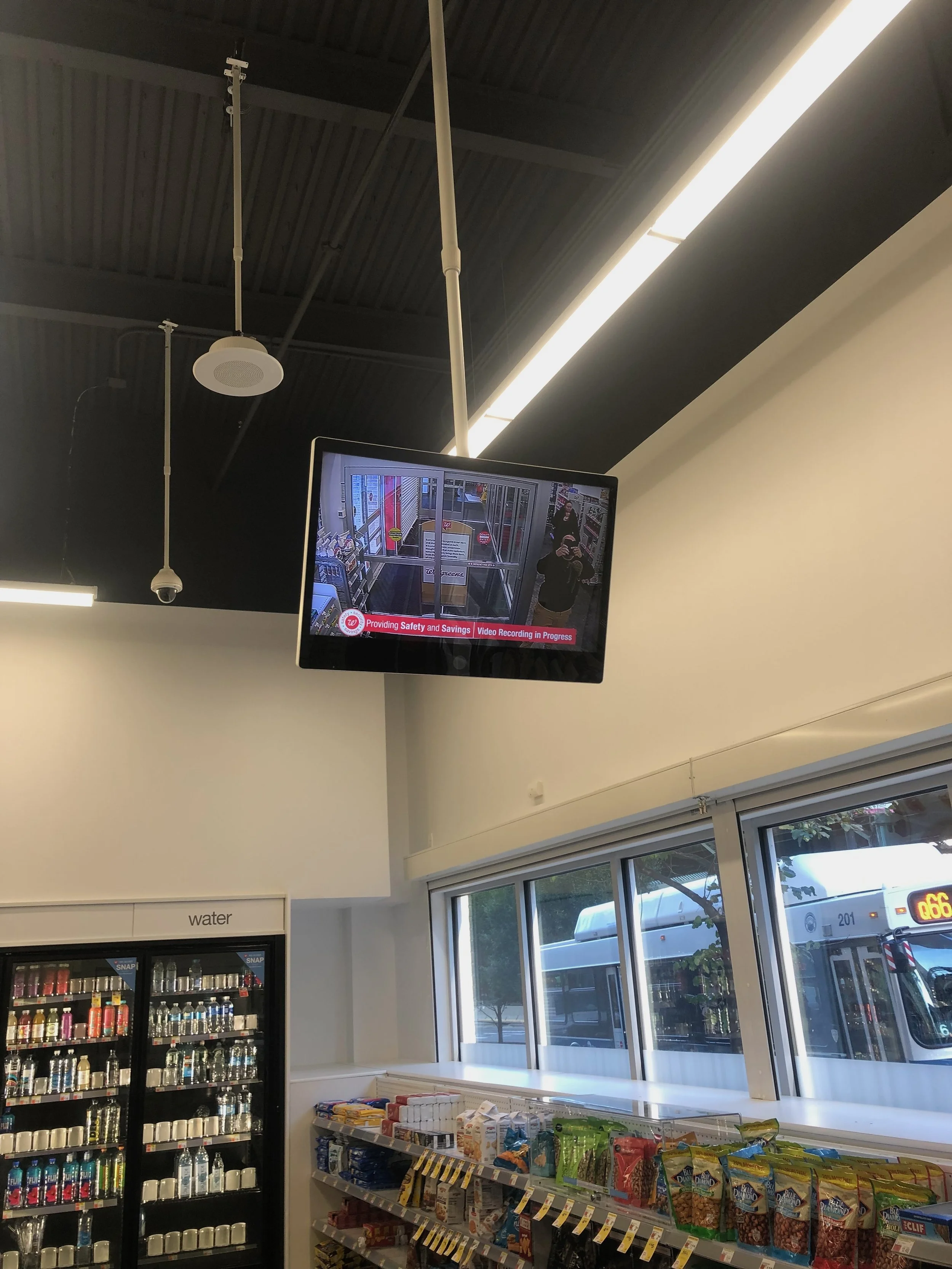 Interior of a convenience store with snack shelves and a TV monitor showing security camera footage.