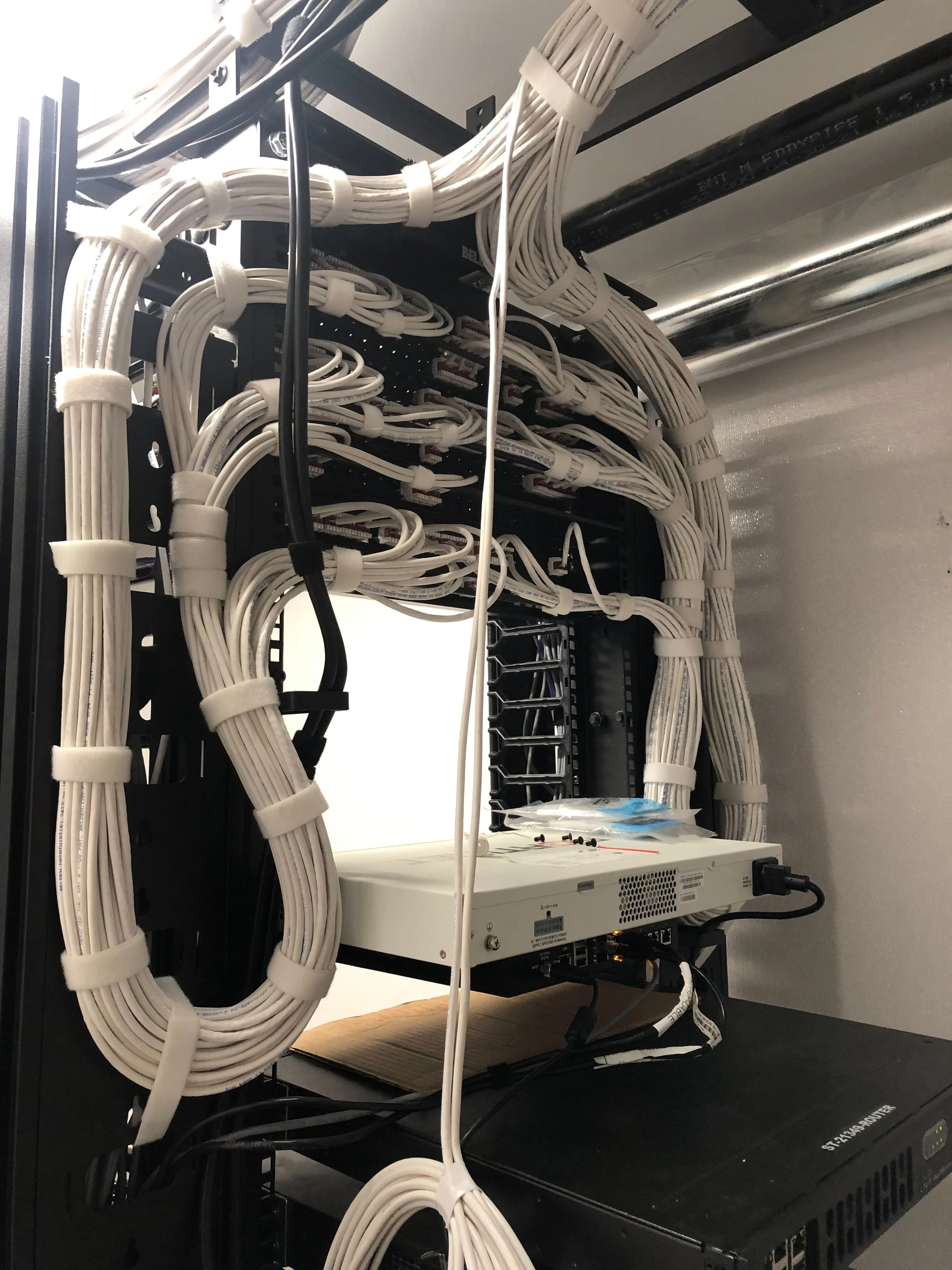 A server rack with numerous white Ethernet cables organized and bundled, connected to network equipment inside. The cables are secured with cable ties and run to various ports on network devices.