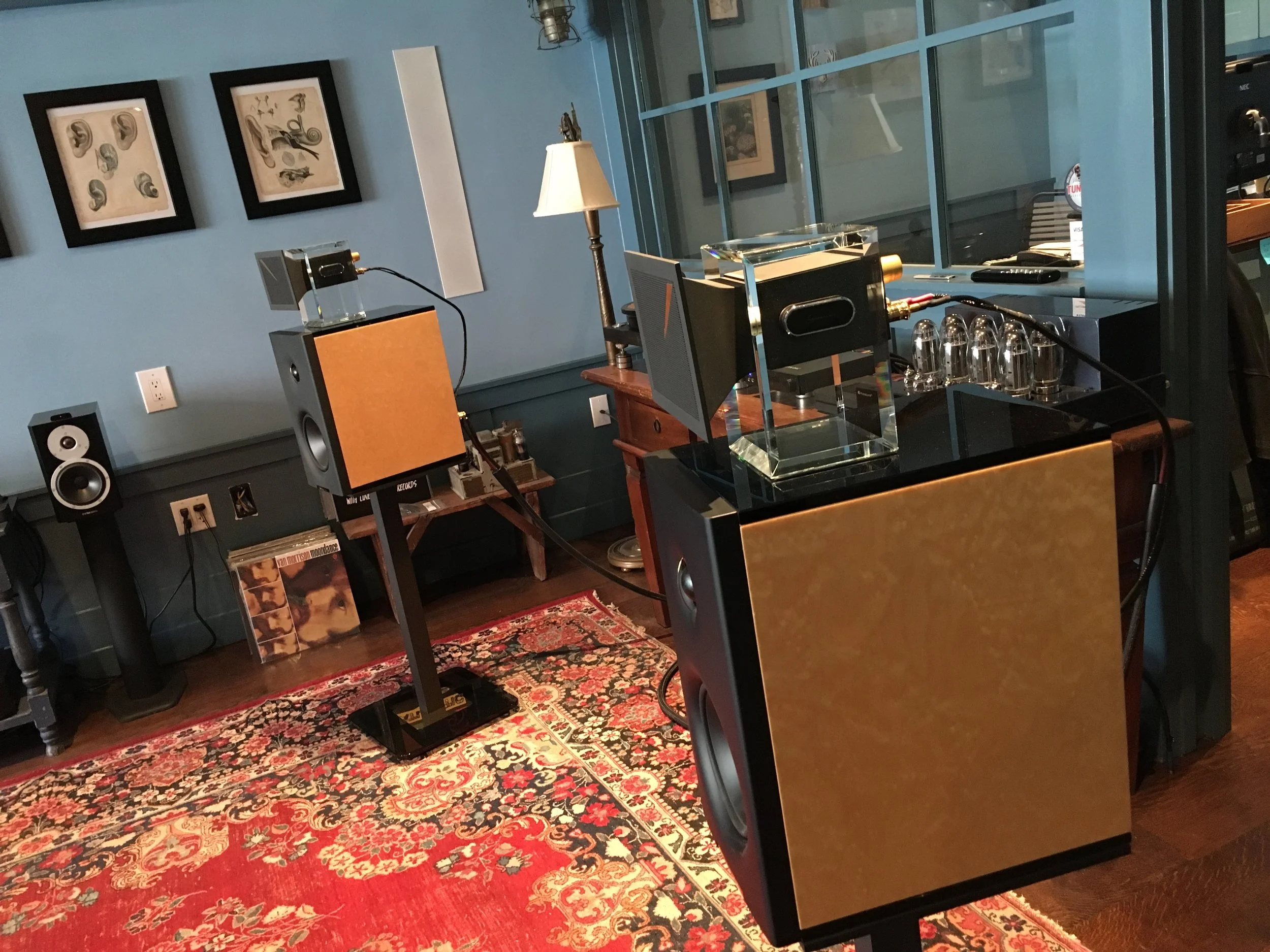 A room with blue walls, framed artwork, a lamp, a wooden table, a piece of audio equipment, and a patterned rug.