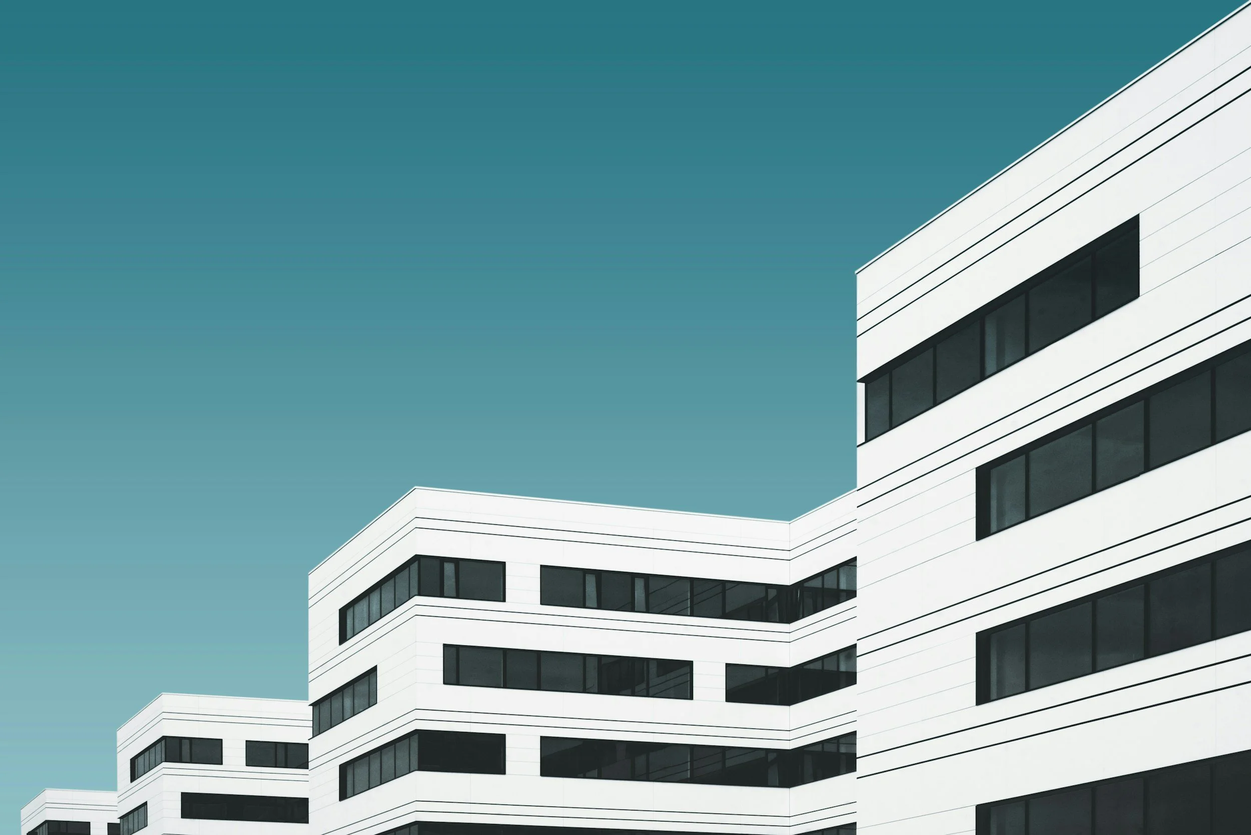 Modern white medical building with large black windows against a clear blue sky.