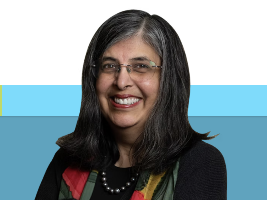 A woman with dark hair, glasses, and a smile, wearing a colorful scarf and a black top, against a digital background with blue and white sections.