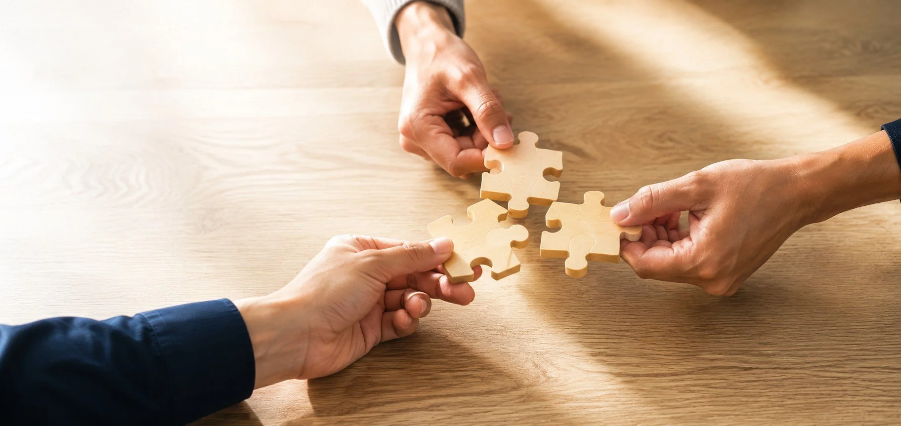Three people connecting wooden puzzle pieces, symbolizing teamwork and collaboration
