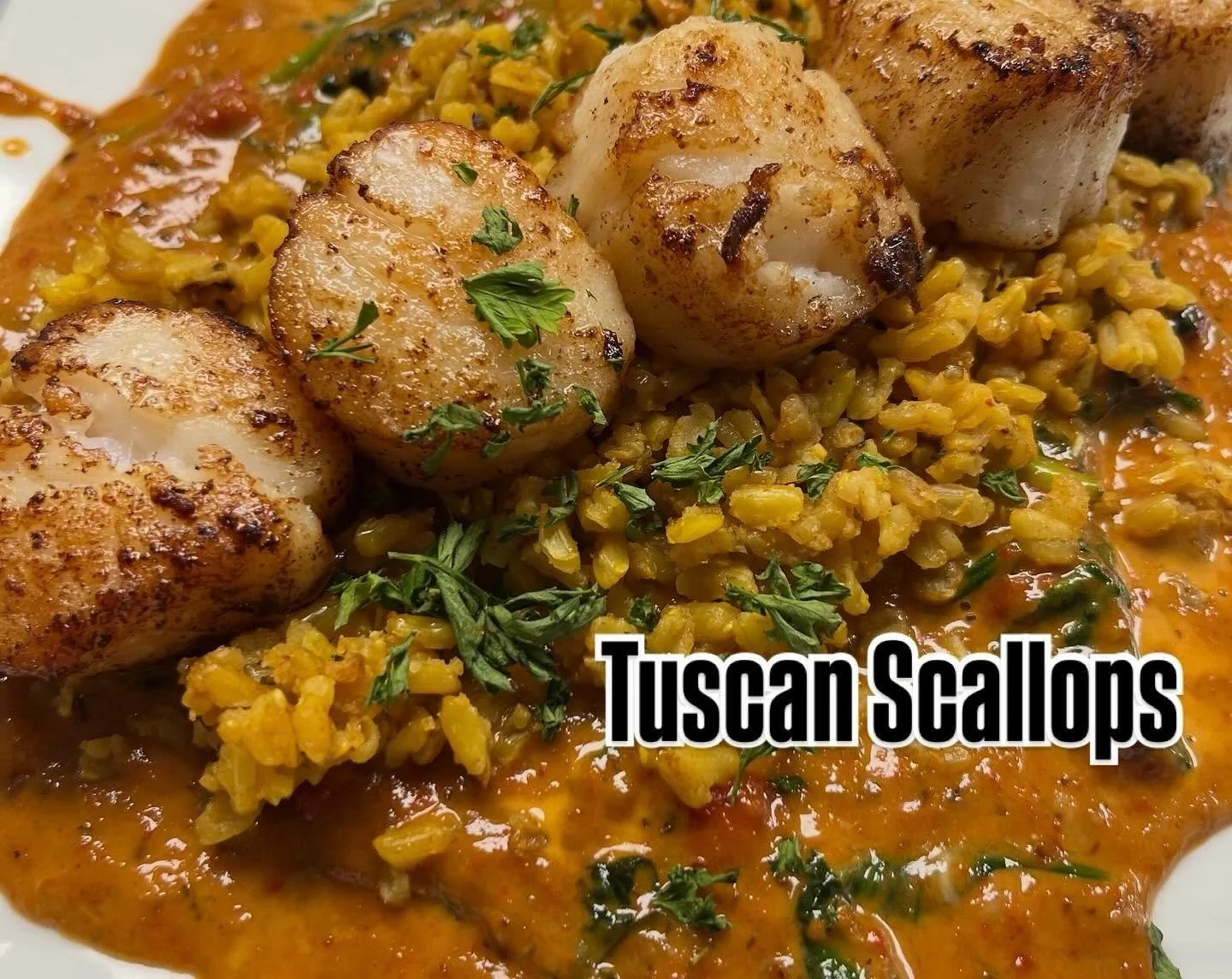 Seared scallops on a bed of yellow risotto garnished with chopped parsley, served with a rich sauce.