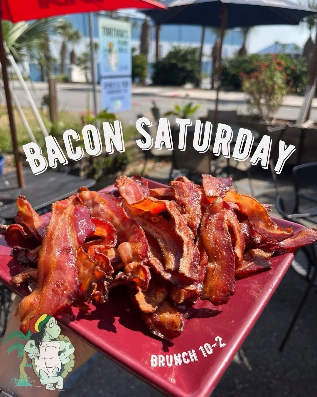 A red plate filled with cooked bacon strips, held outdoors at a patio with tables and umbrellas, with the text "Bacon Saturday" and "Brunch 10-2" overlaid, and a small cartoon character with dreadlocks in the bottom left corner.