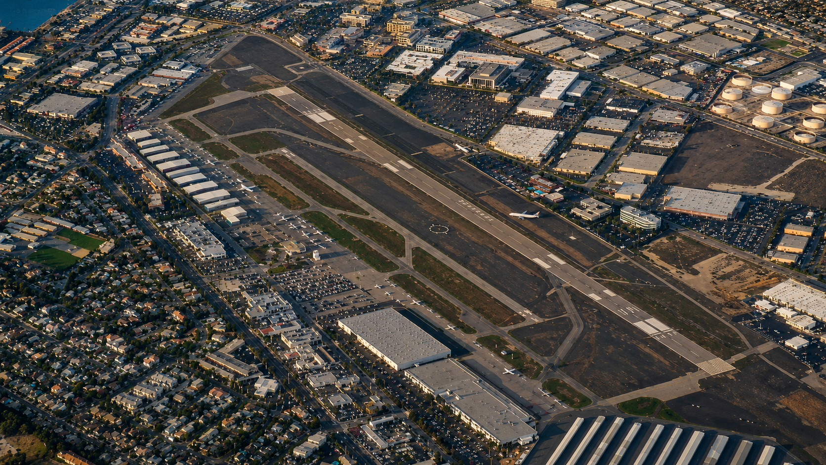 Aerial view of an airport with runways, taxiways, and planes, surrounded by roads, parking lots, and urban buildings.