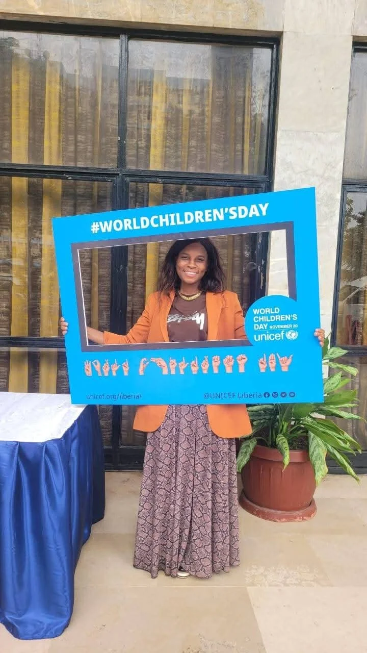 A woman smiling and holding a large blue frame with the hashtag #WORLDCHILDREN'SDAY and the UNICEF logo, celebrating World Children's Day.