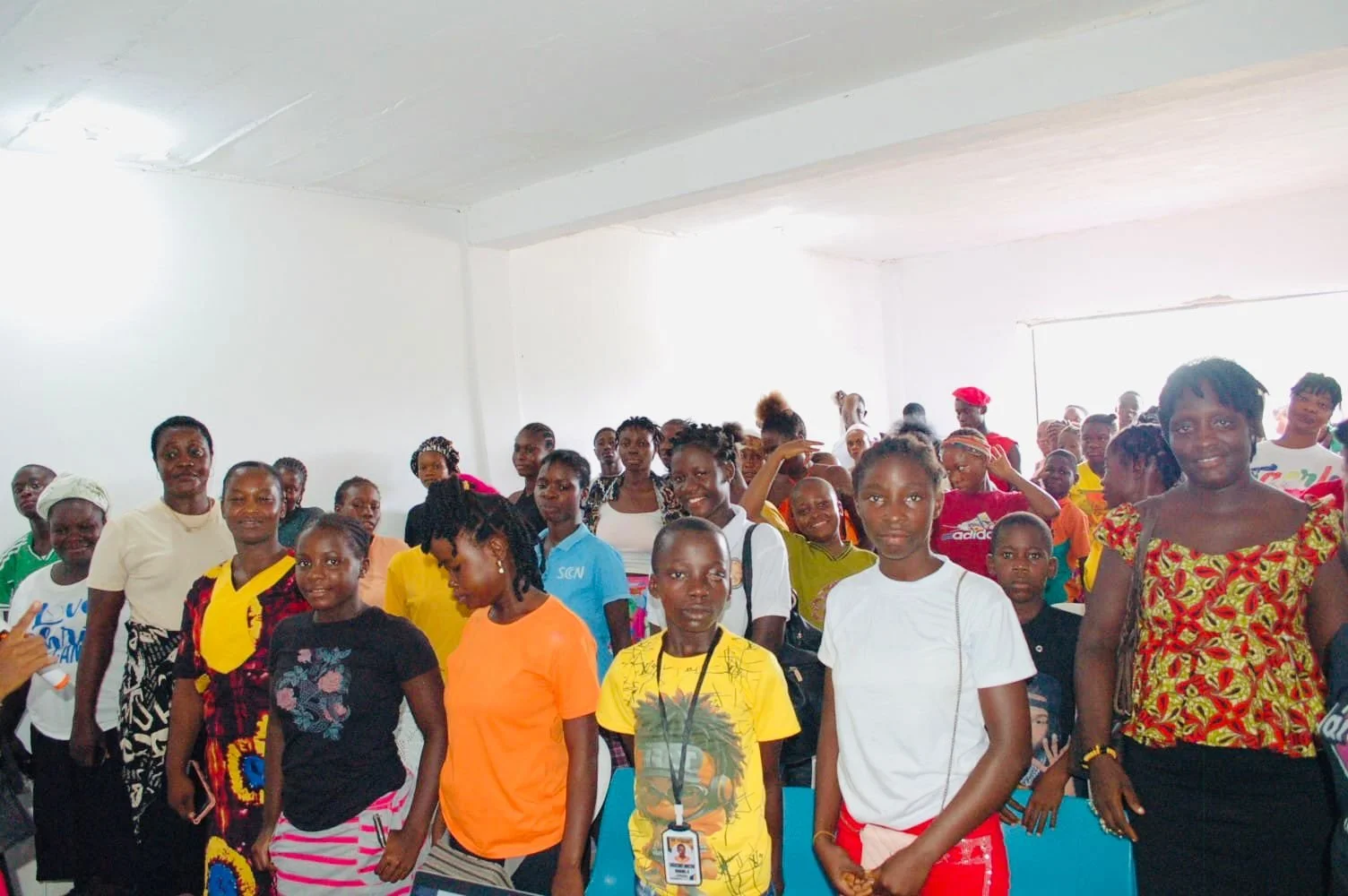 A diverse group of women and children gathered indoors for a community event or meeting, standing and smiling at the camera.