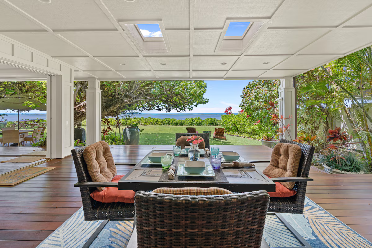 Dining table set for four on covered porch overlooking lush garden and ocean view with trees and plants