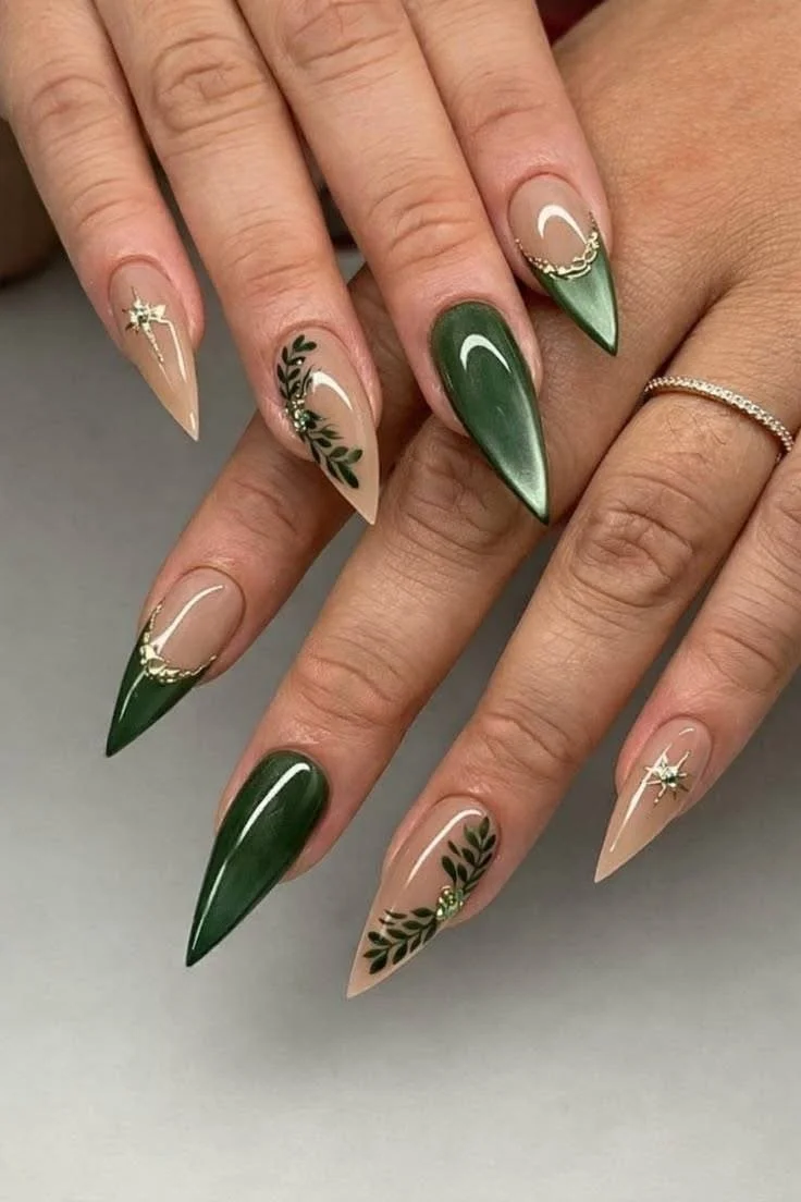 Nail art with green, nude, and clear polish, accented with gold and black leaf designs and small gold embellishments.