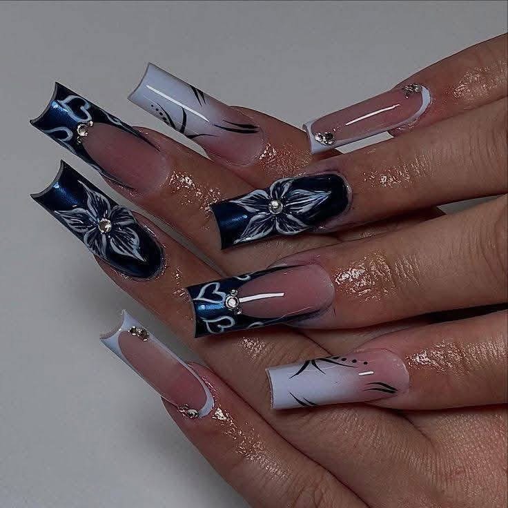Nail art with long square acrylic nails featuring black and white floral designs, hearts, and rhinestones.