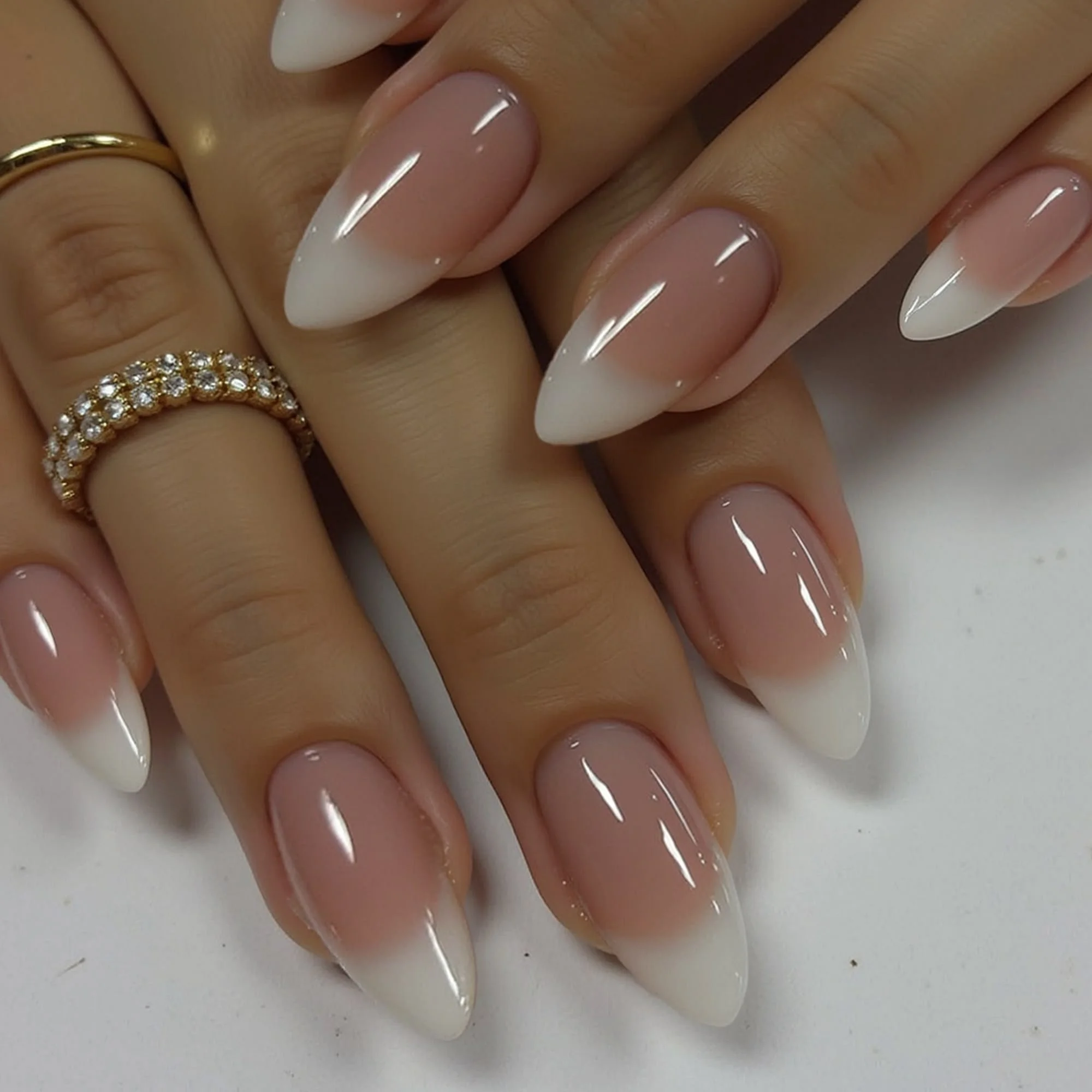 Close-up of a person's hand with long, almond-shaped nails painted with a French manicure design, featuring natural pink base and white tips. The person is wearing a gold ring with small stones on their ring finger.