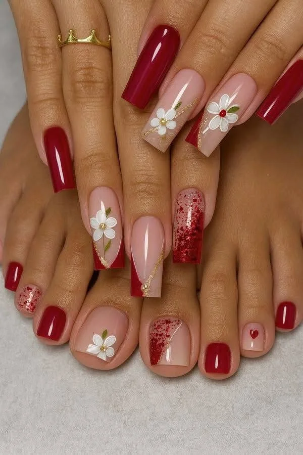 Close-up of hands and feet with manicured nails in red, pink, and floral designs, including glitter and small heart accents.