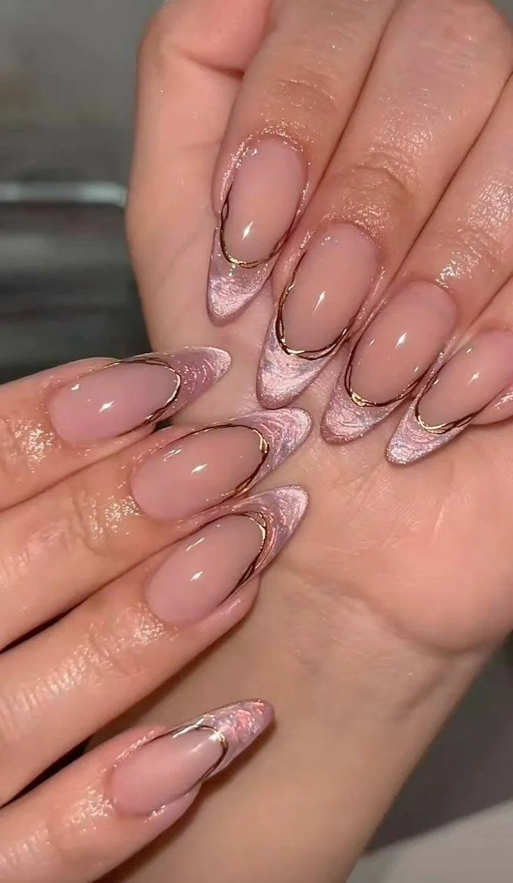 Close-up of a hand with long, almond-shaped nails featuring a pink and silver marble design with gold metallic accents along the edges.