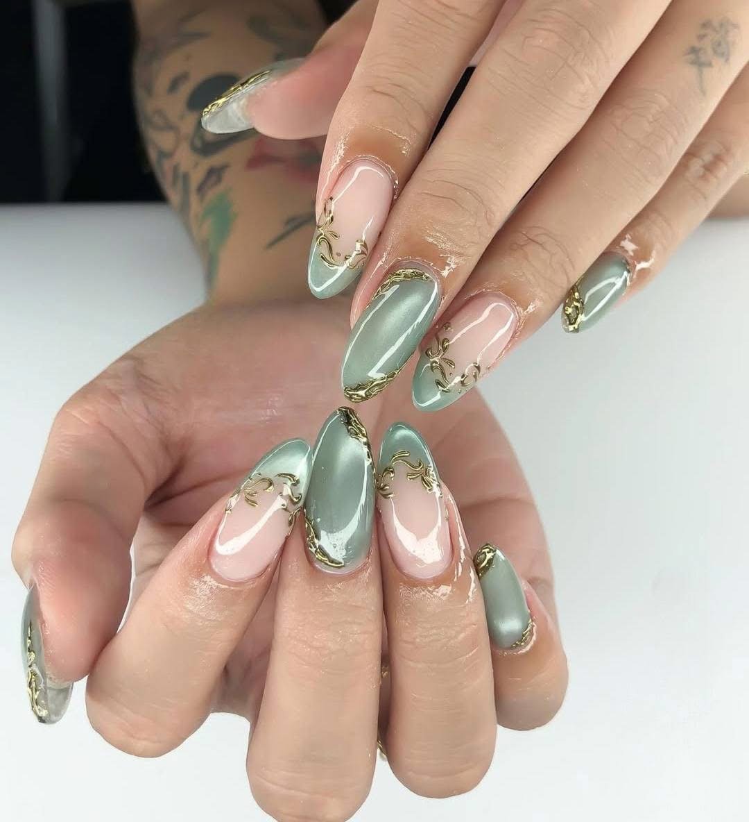 Close-up of manicured nails with pastel green and pink polish, gold detailing, and clear sections.
