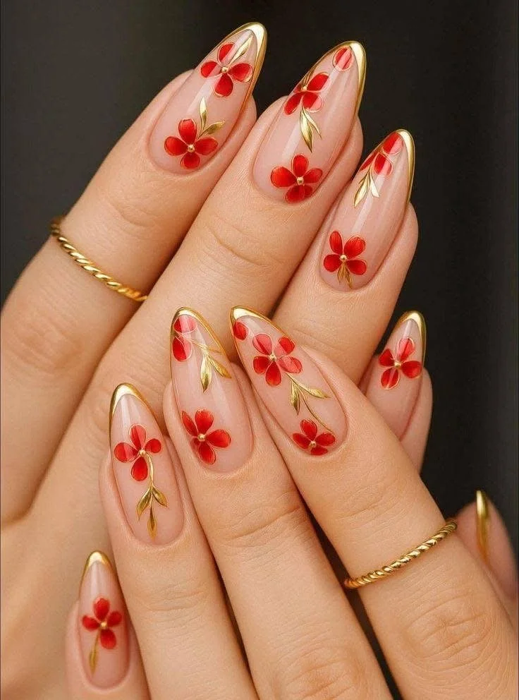 Close-up of manicured nails with red floral designs, gold accents, and clear glossy polish, with gold rings on the fingers.