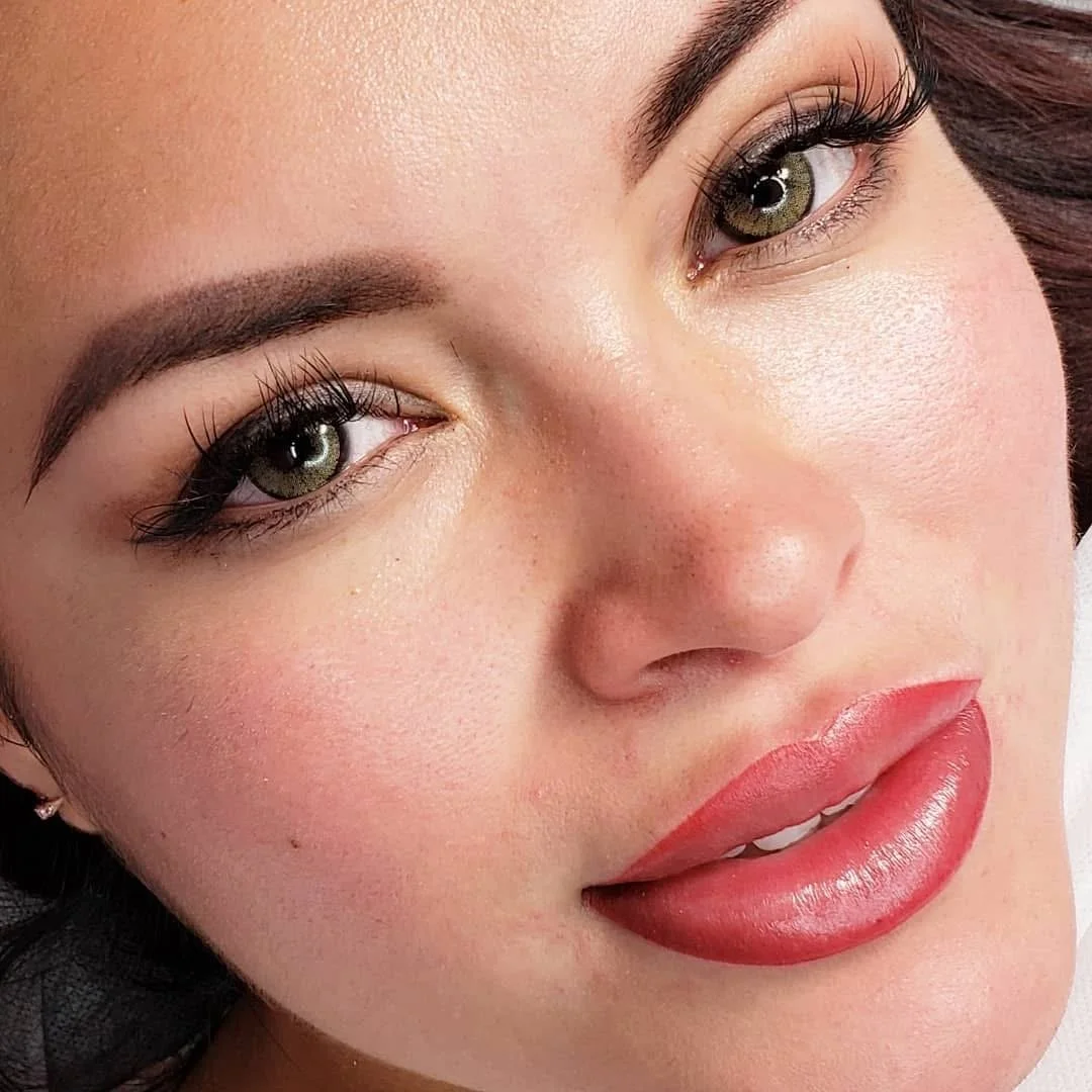 Close-up of a woman's face with green eyes, arched eyebrows, makeup, and red lipstick.