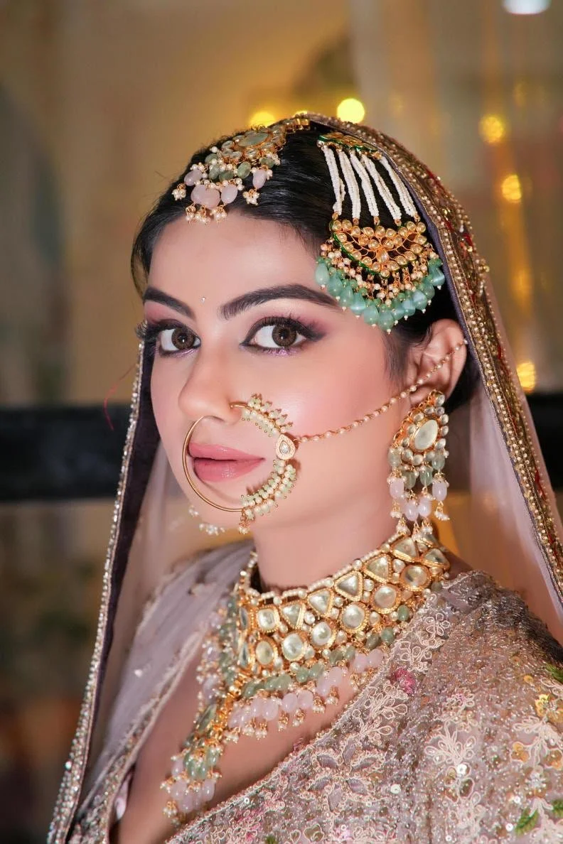 Close-up of a woman wearing traditional Indian bridal jewelry, including a nose ring, forehead ornament, earrings, and layered necklaces, dressed in an embellished saree or lehenga.