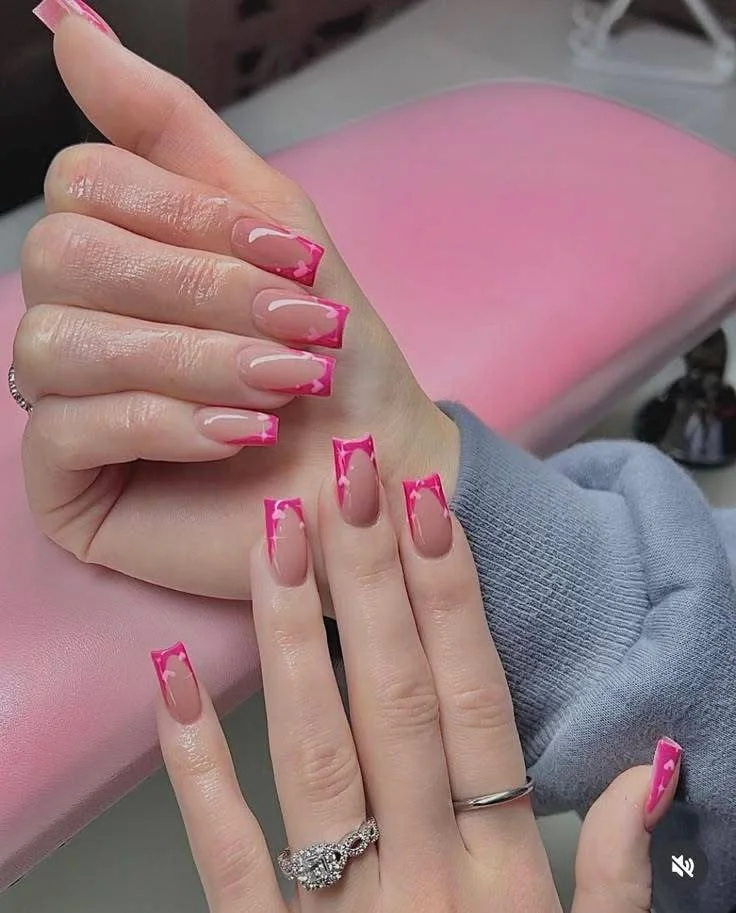 Close-up of hands with freshly manicured nails featuring pink and nude color with pink tips, resting on a pink cushioned surface.