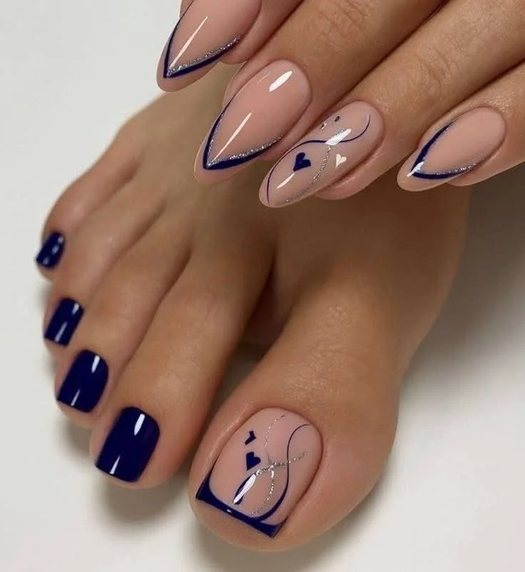 Manicure with navy blue, nude, and silver designs featuring hearts and curved lines on the toenails and fingernails.