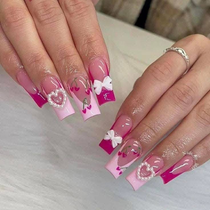 Close-up of hands with decorated long acrylic nails featuring pink, white, and heart motifs, with some nails adorned with white bows and pearl hearts.