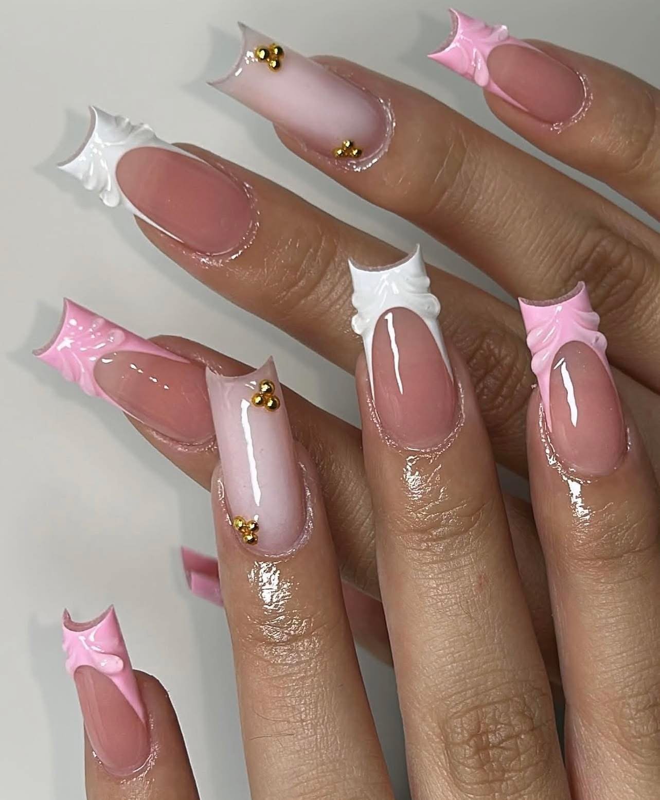 Close-up of decorated acrylic nails featuring pink and white French tips with pearl-like embellishments and gold accents.