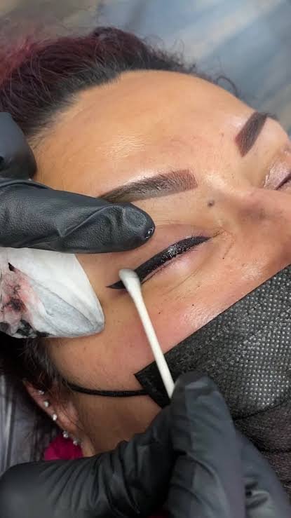 Close-up of a woman receiving a cosmetic eyelash tinting or dye procedure, with a technician applying dye near her closed eye.
