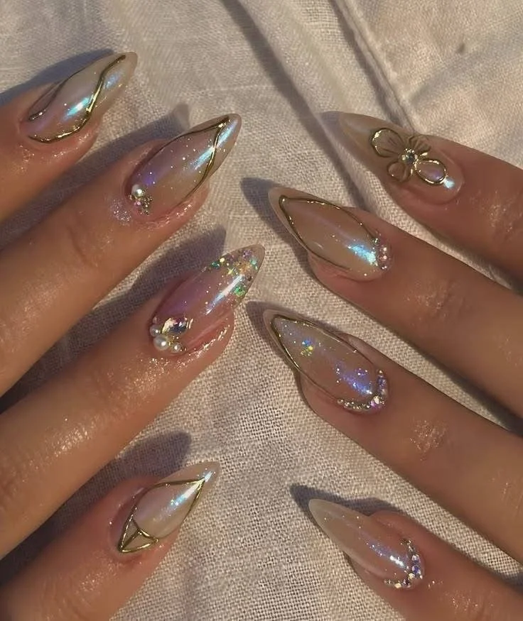 Manicured nails with iridescent, glossy finish, gold accents, and decorative pearls and rhinestones.