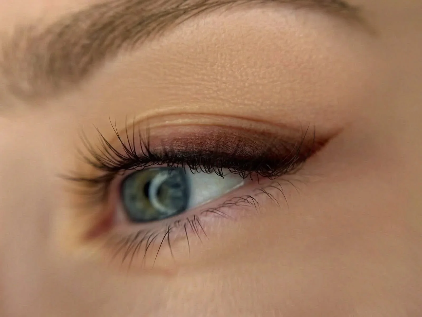 Close-up of a person's eye with blue iris, long lashes, and makeup on eyelid.