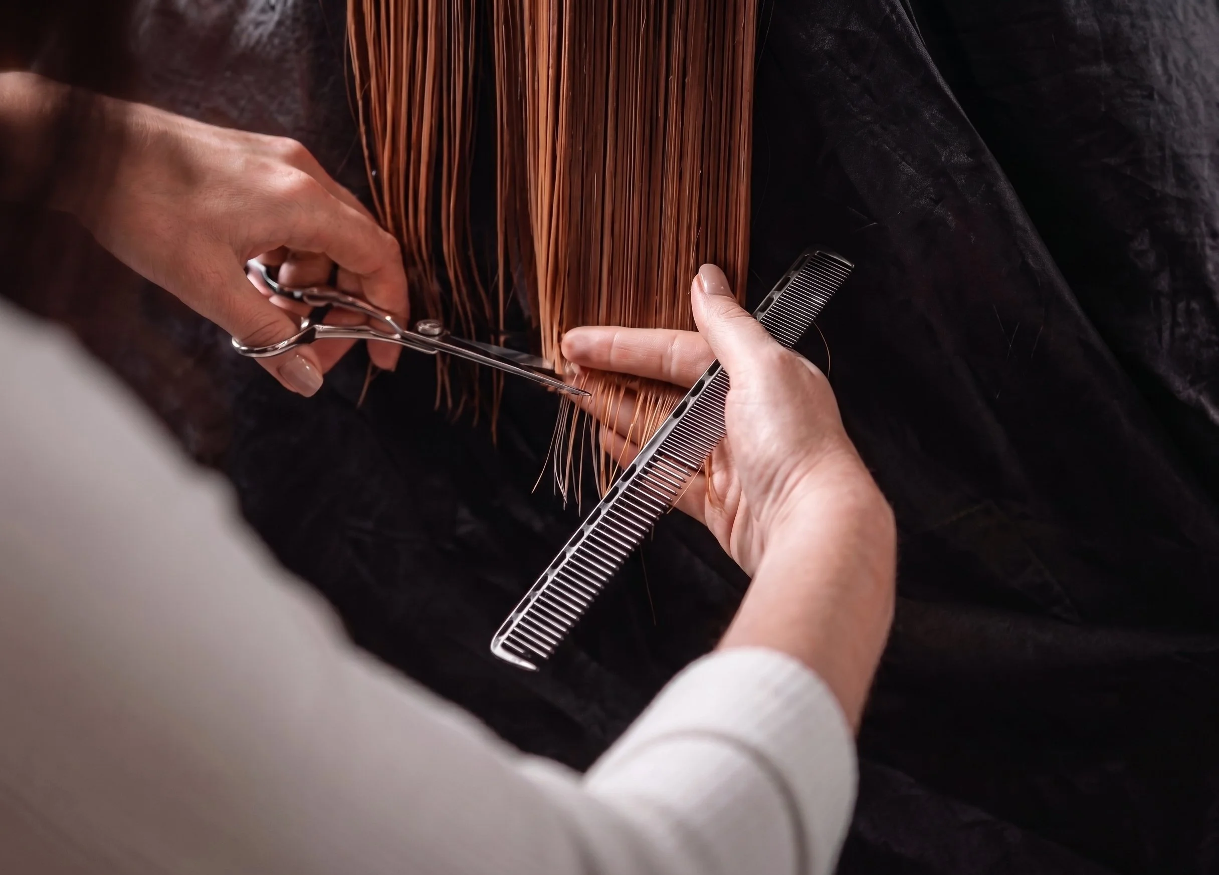 A person trimming brown hair with scissors and a comb during a haircut.