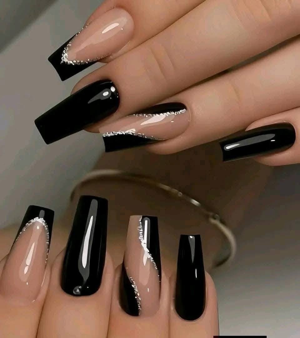 Hand with long, manicured nails painted in black with natural accents and silver glitter tips, holding a gold bracelet.