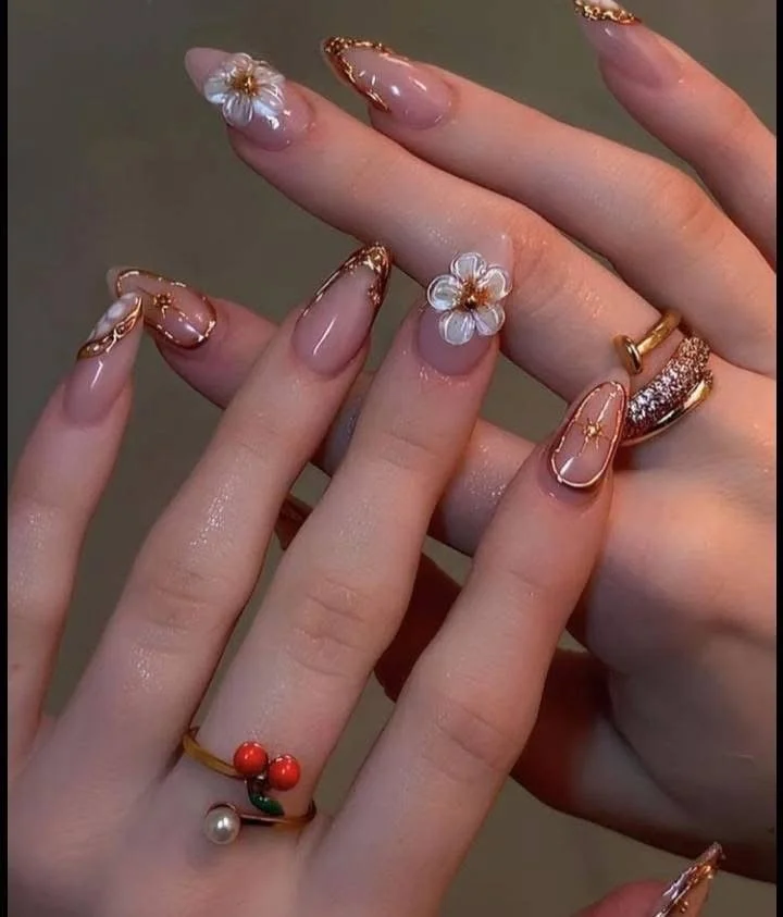 Close-up of hands with decorated nails and rings, featuring floral nail art and shiny details.