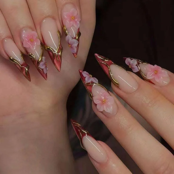Close-up of manicured nails with intricate pink floral designs, gold accents, and a glossy finish.