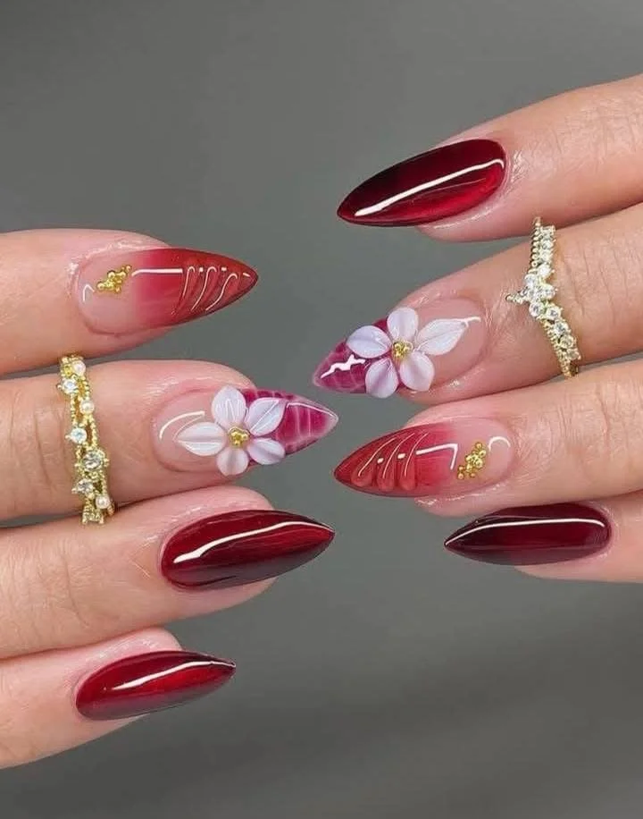Close-up of manicured nails with red, marbled, and floral nail art, and gold rings on fingers.