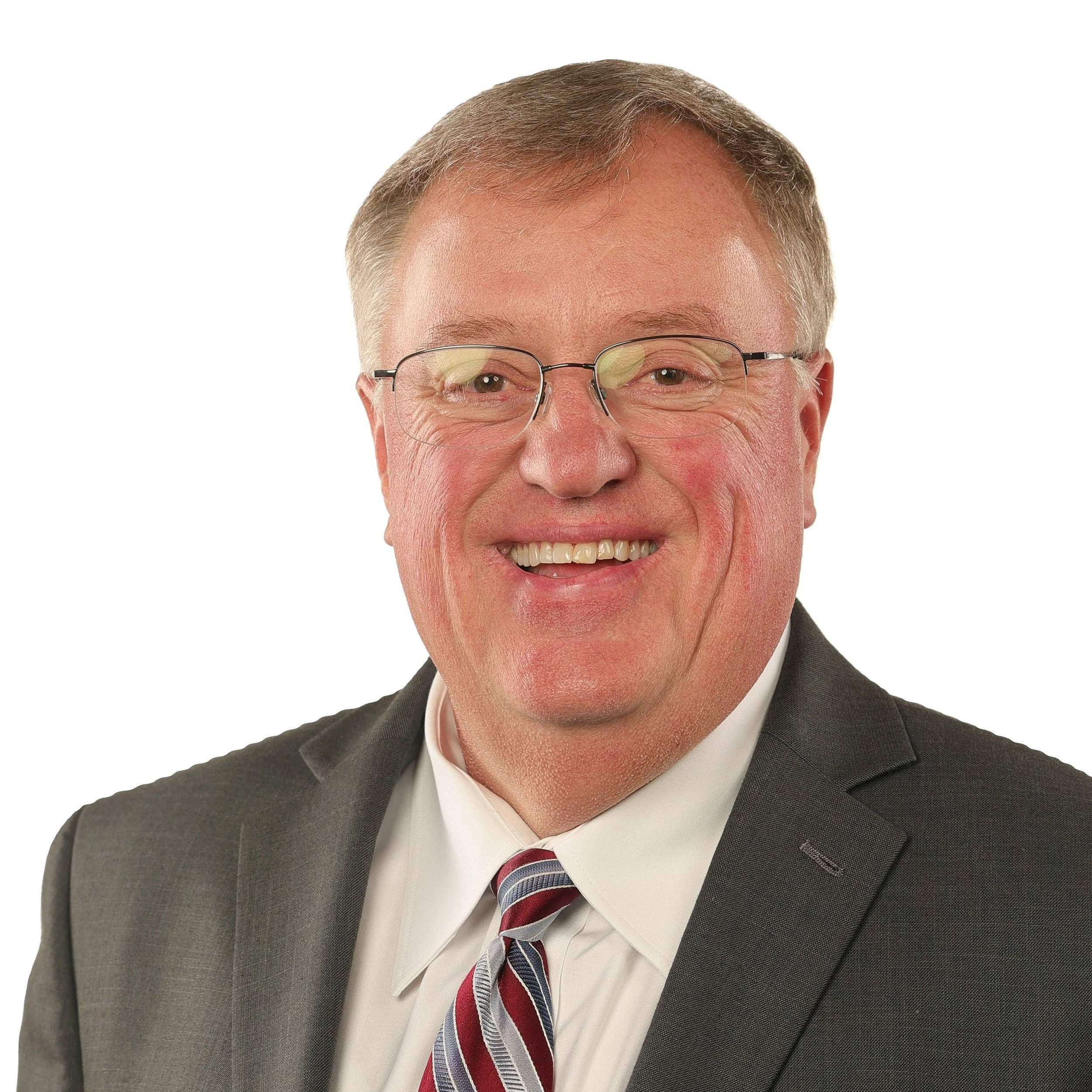 Close-up of a smiling middle-aged man wearing glasses, a dark suit, a white shirt, and a striped tie, against a white background.