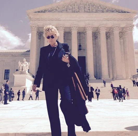 A woman standing in front of the U.S. Supreme Court building, holding a coat and a cellphone.