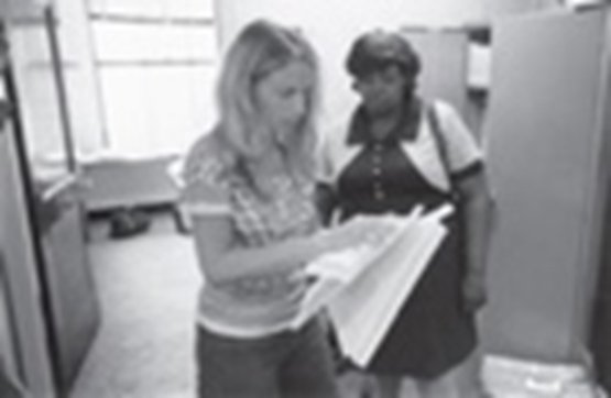 Two women standing in an office, looking at a document or magazine together.