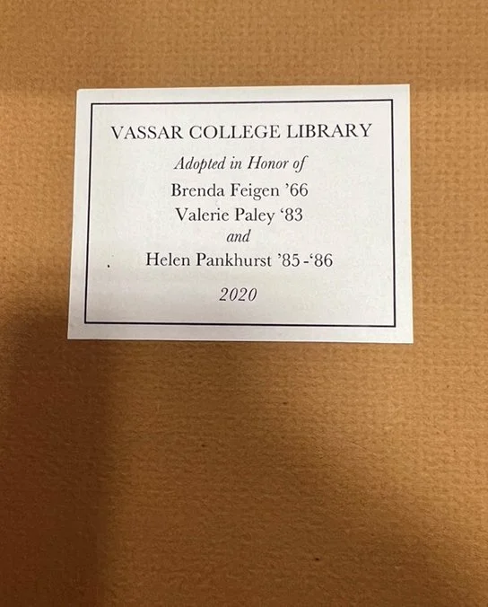 A white paper plaque with black text mounted on a beige wall, dedicated to individuals in honor of their contributions to the Vassar College Library, dated 2020.