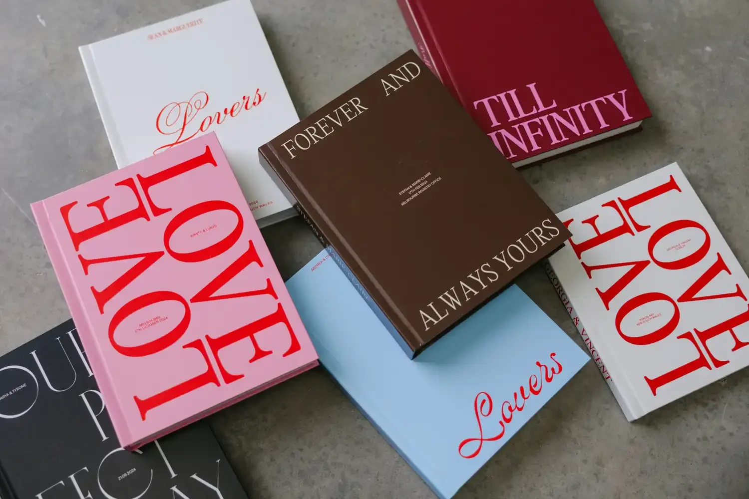 Multiple books on a gray surface, with titles such as "Love," "Forever and Always Yours," and "Till Infinity."