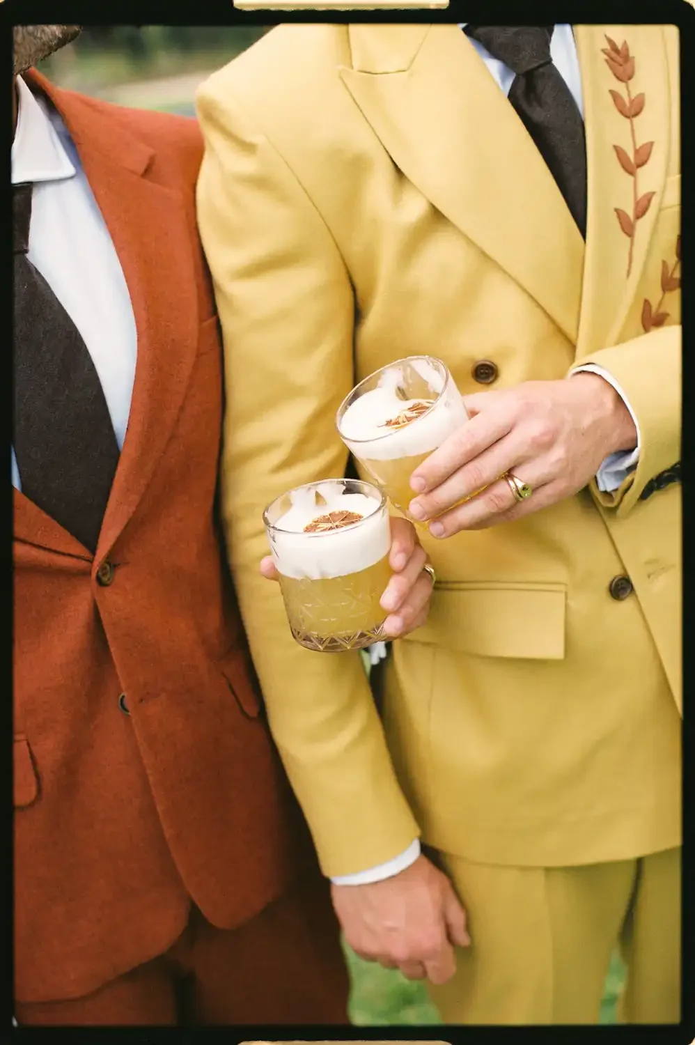 Two people dressed in colorful suits holding glasses of beer with foam on top, close-up shot.