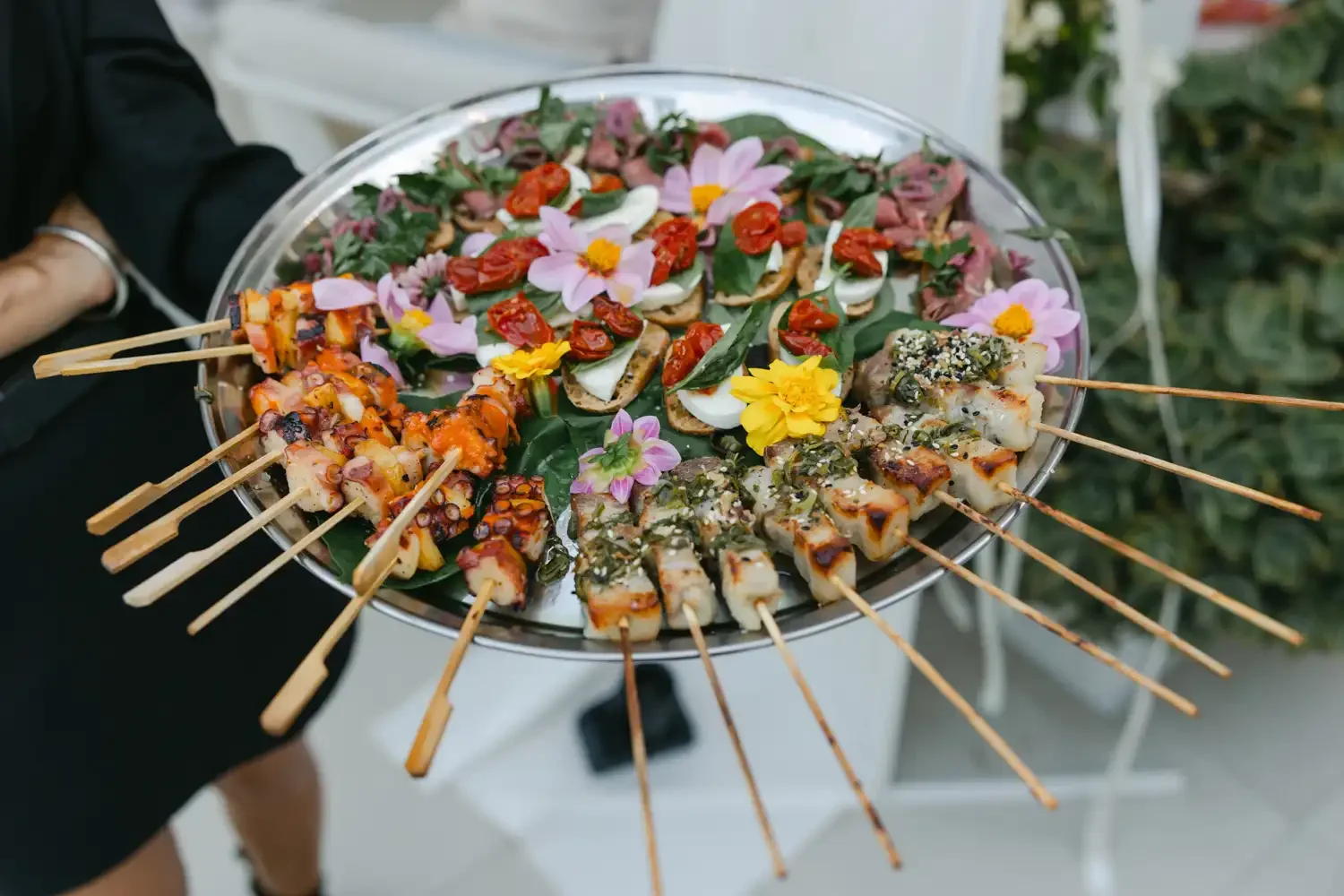 Tray of assorted skewered Asian appetizers with flowers and greenery for decoration.