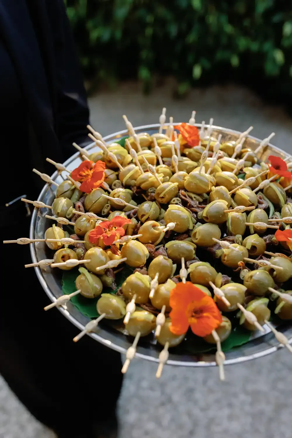 A tray filled with skewered green olives and orange edible flowers.