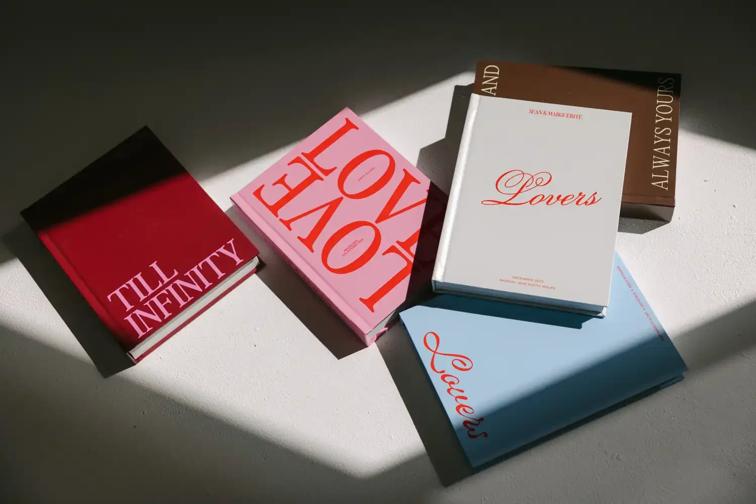 Five books with colorful covers arranged on a white surface, with light and shadow creating contrast.