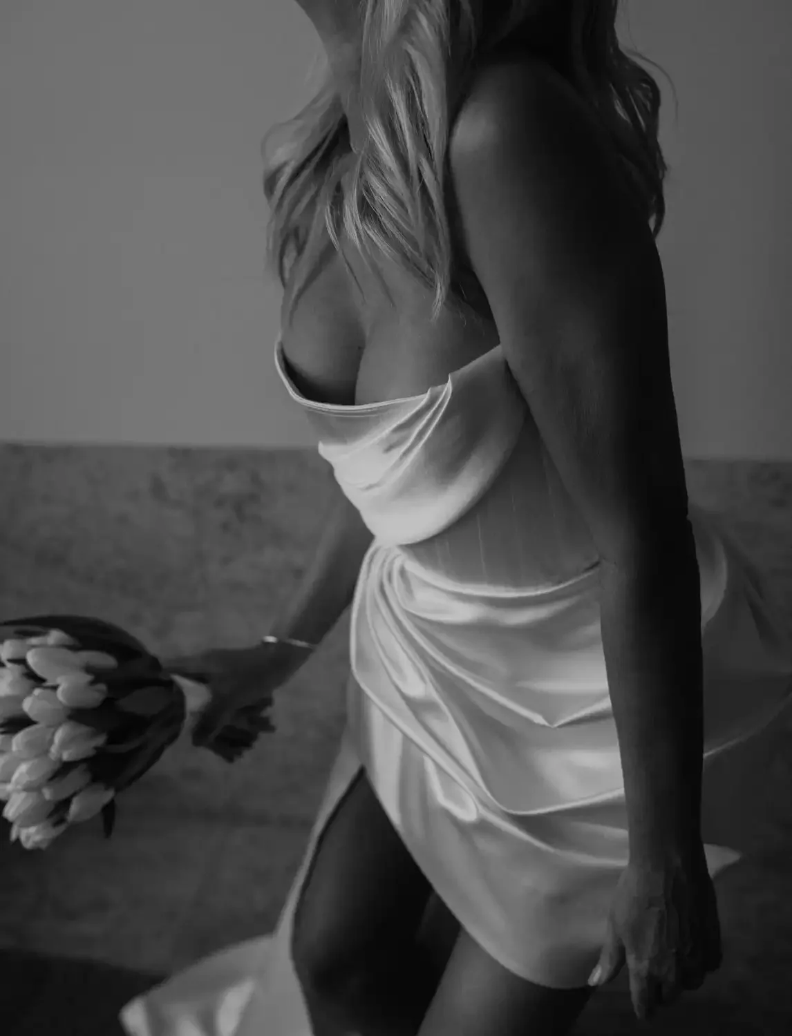 Black and white photo of a woman with long, wavy hair wearing a satin slip dress and holding a bouquet of tulips.