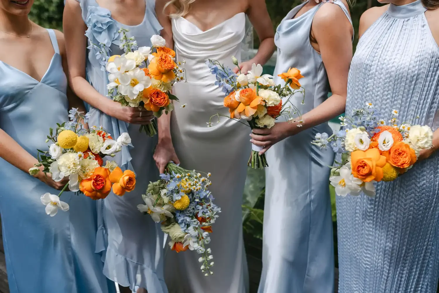 Group of women in pastel dresses holding colorful flower bouquets at an outdoor event.
