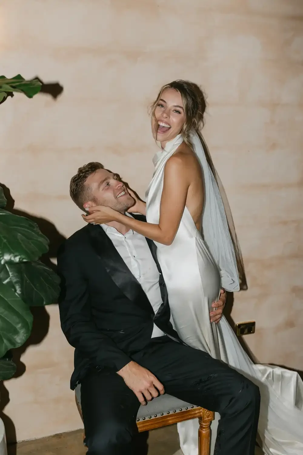 A happy woman in a white satin dress and a man in a black suit and white dress shirt, smiling and embracing each other in a joyful moment.