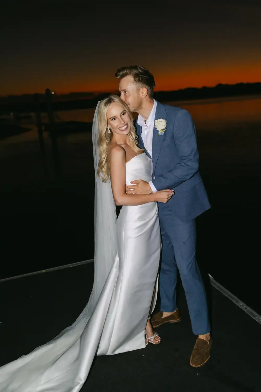 A bride and groom on their wedding day at sunset, smiling and embracing each other outdoors.