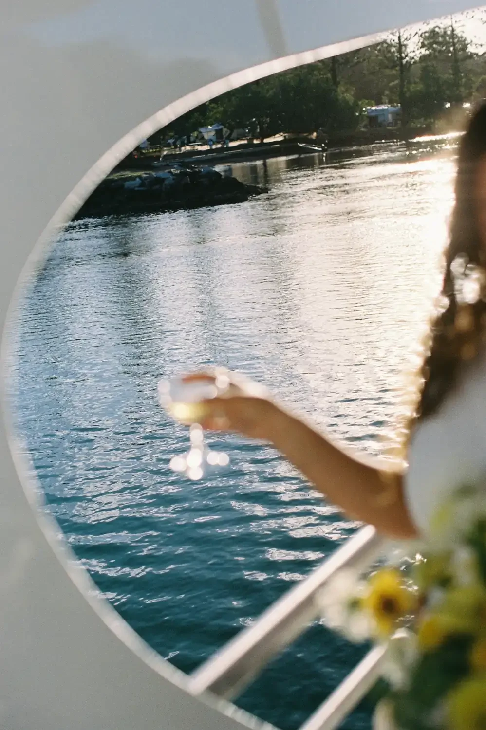 View of a river during sunset seen through a boat's porthole, with a blurred part of a person and some flowers visible on the boat.