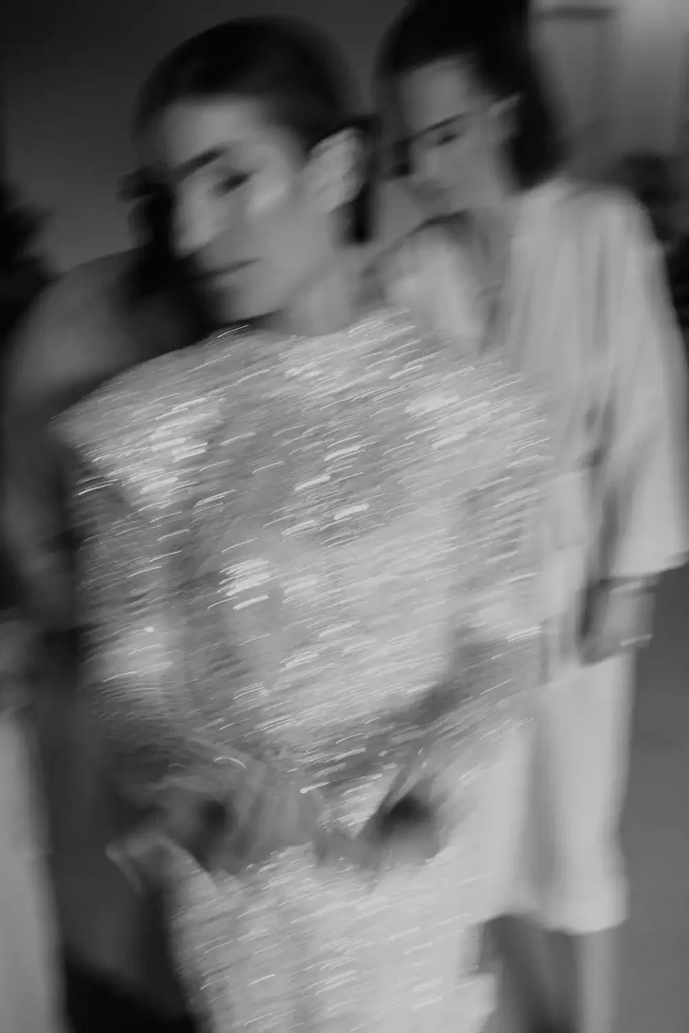 Two people holding a large, shiny, textured object with a blurred background, grayscale photograph.